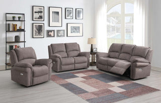 A modern living room featuring the Annaghmore Wentworth Clay 3 Seater Recliner Sofa in velvet with electric recline, a geometric area rug, side table with lamp, large window, and gallery wall. Natural light brightens the space.
