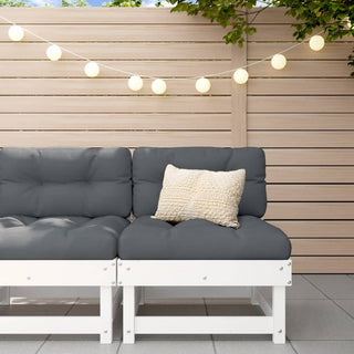 The vidaXL Middle Sofa with Cushions (White, Solid Pine Wood) sits against a light wooden fence with dark gray cushions and a textured beige pillow. String lights hang overhead, and green leaves are visible above.
