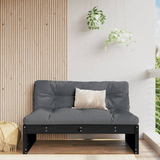 A modern balcony features the vidaXL Middle Sofa Black 120x80 cm Solid Wood Pine, a light textured pillow, wooden slat accent wall, hanging green plants, and a beige woven basket. Natural light brightens the space.