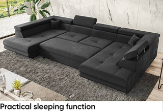 The SOFAINSTORE Tivoli U-Shaped Fabric Corner Sofa Bed by Sliding Sofas, a 7-seater in grey with storage, modular design, and adjustable headrests, stands on a gray rug amid a marble wall, potted plant, and glass coffee table—uniting style and function.