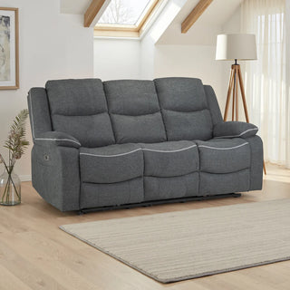 A modern living room features the Beehive Furniture SOFAINSTORE Harald Grey Fabric Electric Recliner Sofa – 3 Seater with dual power recline and contrast stitching, set on light wood floors, a beige rug, floor lamp, plant vase, and large sunlit windows.