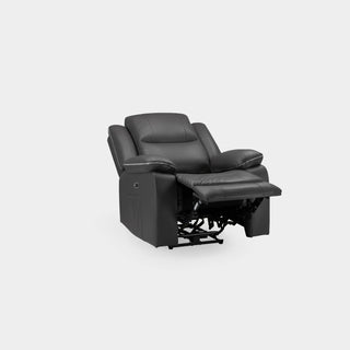 A modern living room features the Beehive Furniture SOFAINSTORE Harald Black Leather Electric Recliner Armchair with power recline and contrast stitching on a light wood floor and beige rug, accented by a lamp, white curtains, framed art, and a vase by the window.