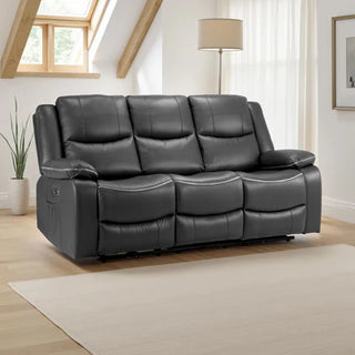 A modern living room with the Beehive Furniture SOFAINSTORE Harald Black Leather Electric Recliner Sofa (3 Seater, dual power recline, contrast stitching), light wood floors, beige rug, floor lamp, potted plant, and sunlit large windows.
