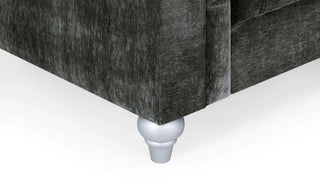 Close-up of the corner of the Beehive Furniture Jubilee Charcoal Grey Velvet Sofa, a 3-seater with button-tufted design and shiny rounded white leg, set against a white background—an elegant living room piece.