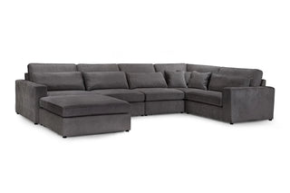 The Kiana Modular Sofa by Beehive Furniture is a large corner design in grey fabric, featuring wide armrests, plush cushions, and an attached left-side chaise lounge for versatile modular seating.