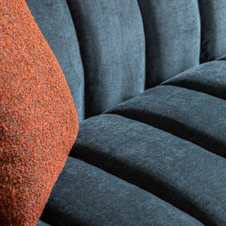Close-up of the Gallery Direct Coste Fabric 3 Seater Sofa in blue upholstery, retro design and comfort, with visible tufting and stitching, featuring an orange textured cushion on the left side.