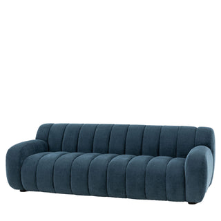 The Gallery Direct Coste Fabric 3 Seater Sofa features blue upholstery, retro design with rounded edges, and vertical channel tufting on the back and seat, styled against a white background.