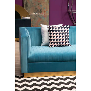 The Premier Sofas Contemporary Light Blue Velvet 3 Seater Sofa with a gold base and tufted design sits on a black and white zigzag rug, accented by one white and one geometric black-and-white pillow, against a purple wall.