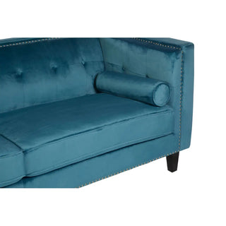 A close-up of the Premier Sofas Felisen Upholstered Velvet 3 Seater Sofa in Blue Elegance, featuring a tufted backrest, cylindrical bolster pillow, nailhead trim, and dark wooden legs.