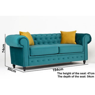 The PF Sofas SOFAINSTORE Florencia 2 Seater Chesterfield features ocean teal velvet fabric, scroll arms, button tufting, black legs, and two yellow accent pillows. Size: 194x90x74cm; seat height 47cm, seat depth 54cm.