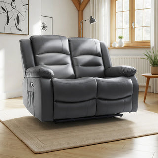 The Beehive Furniture SOFAINSTORE Arclay Black Leather Recliner Sofa – 2 Seater, featuring electric comfort and deep cushion support, sits on a beige rug in a bright living room with wooden floors, large windows, a potted plant, lamp, and abstract wall art.