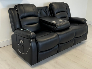 The Beehive Furniture SOFAINSTORE Arclay Black Leather Recliner Sofa – 3 Seater features electric recline, a drop-down cupholder console, and built-in charging—ideal for luxury comfort on light wood flooring and against a white wall in UK homes.