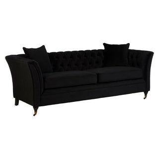 The Dartford 3 Seater Sofa by Nestium features onyx black velvet, flared arms, two seat cushions, matching throw pillows, and short legs with elegant front brass casters for a refined look.
