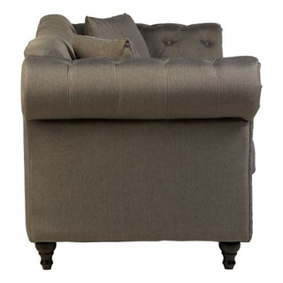 Side view of the Nestium SOFAINSTORE Kensington Grey Fabric Chesterfield Sofa – 2 Seater, showing scroll arms, button back, studded detail, and dark wooden legs. A matching cushion highlights its elegant design.