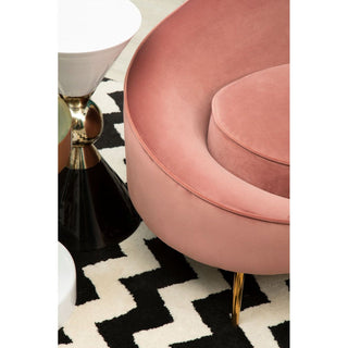 The Crescent Salmon Pink Velvet Sofa from Premier Sofas features a luxurious curved 4 seater design with gold legs, shown alongside modern black and white side tables on a zigzag rug—perfect for elevating your living room style.