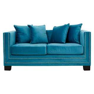 The Pipirima Upholstered Velvet 2 Seater Sofa by Premier Sofas features plush cyan blue fabric, four matching square cushions, silver nailhead trim on the arms and base, and short black legs for a stylish touch.