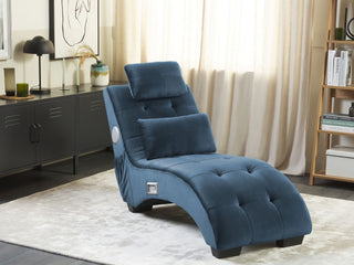 The Beliani SOFAINSTORE Blue Velvet Fabric Chaise Lounge, featuring tufted upholstery, Bluetooth speakers, USB charging port, and a cushioned headrest, sits on a light rug near a shelf and sideboard in a bright living room with sheer-curtained windows.