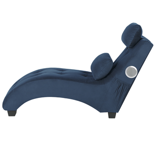 The Beliani SOFAINSTORE Blue Velvet Fabric Chaise Lounge features tufted upholstery, a curved design, cushioned headrest, short black legs, two pillows, inbuilt Bluetooth speakers, and a USB port. Shown from the side on a white background.